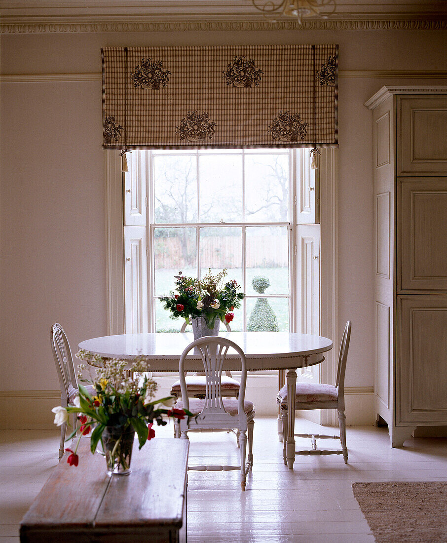 White dining table and chairs at window in white room with high ceiling