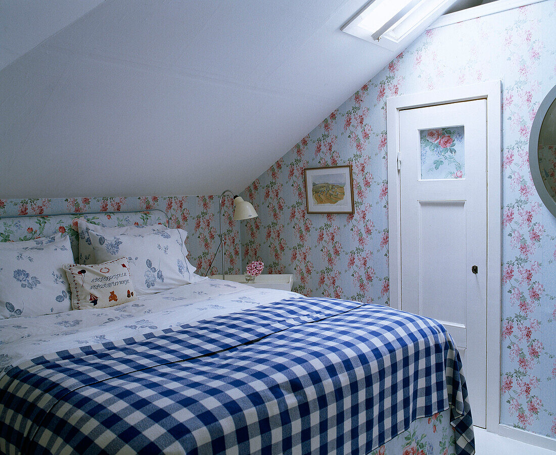 Doppelbett mit blau kariertem Bezug in einem Schlafzimmer mit Blumentapete