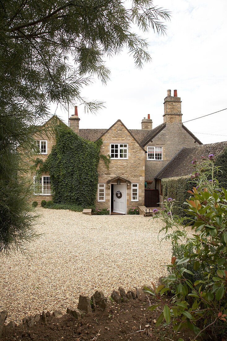 An exterior of a country house with gravel drive shrubs and trees front door open