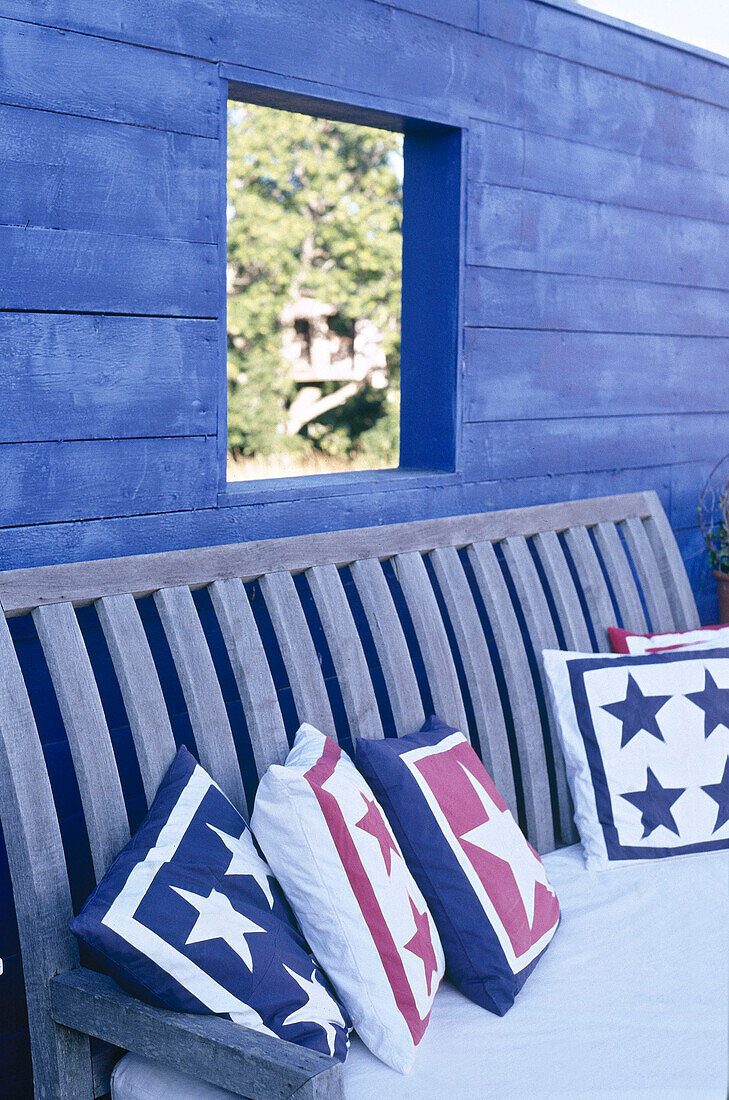 Wooden bench and cushions in front of blue painted timber wall