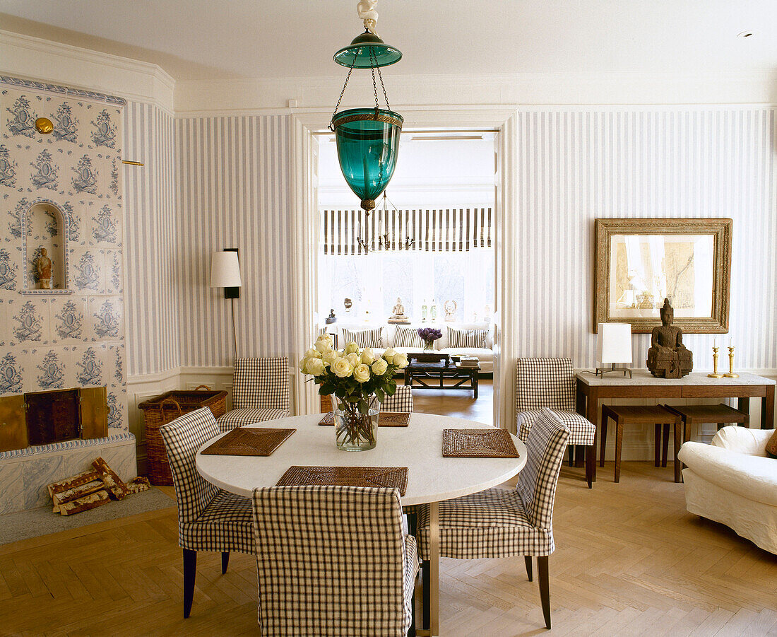 Round table with check pattern chairs in dining room with traditionally Swedish ceramic tiled stove