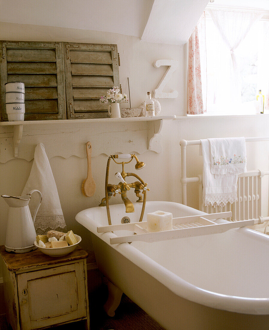 A detail of a country bathroom in neutral colours freestanding bathtub jug cupboard radiator towel shelf