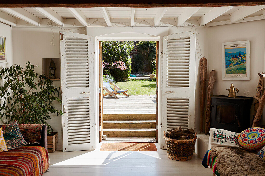 Blick durch die weiß gestrichenen doppelten Fensterläden in den Garten eines Hauses in Bridport, Dorset, UK