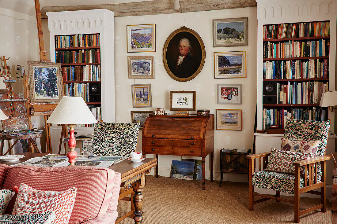 Framed pictures and bookcase with antique bureau and upholstered chair in 17th century Hampshire home, UK