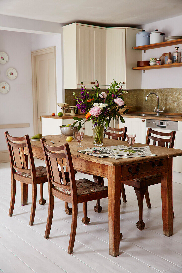 Cut flowers and newspaper on wooden table with chairs in kitchen of 17th century Hampshire home, UK