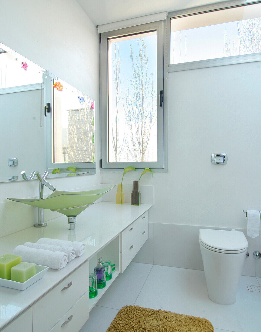 Contemporary white bathroom with large mirror and coloured glass sink and view to outside