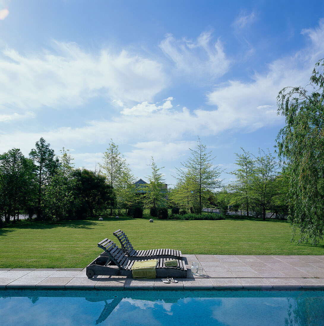 Pair of wood slatted sun loungers in garden beside the pool with lawn in background