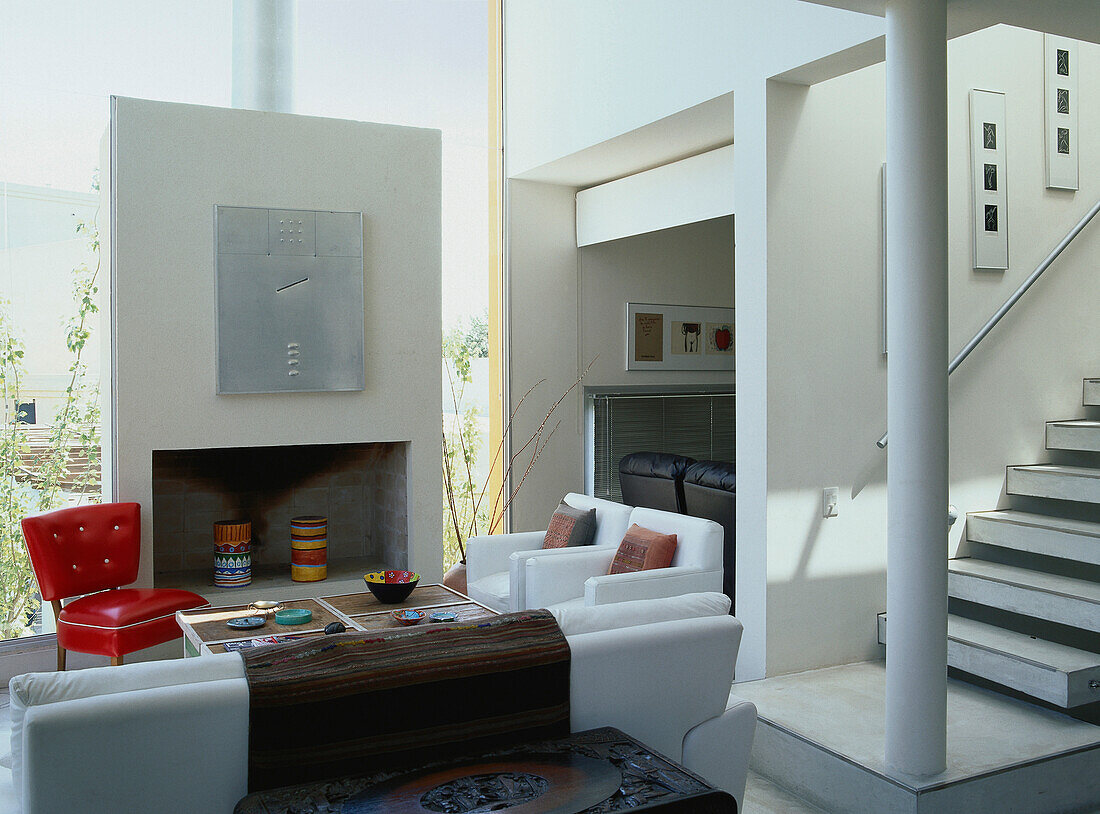 1960s red chair with painted wood coffee table at concrete fireplace with aluminium art piece and double height windows