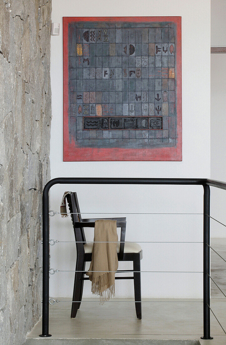 Chair with throw under artwork in hallway with railing and exposed stone wall