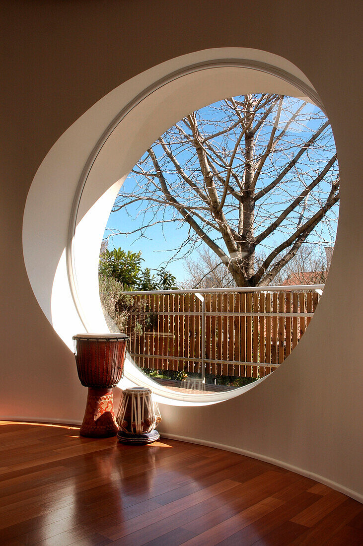 Drums at large circular window in room with red eucalyptus flooring