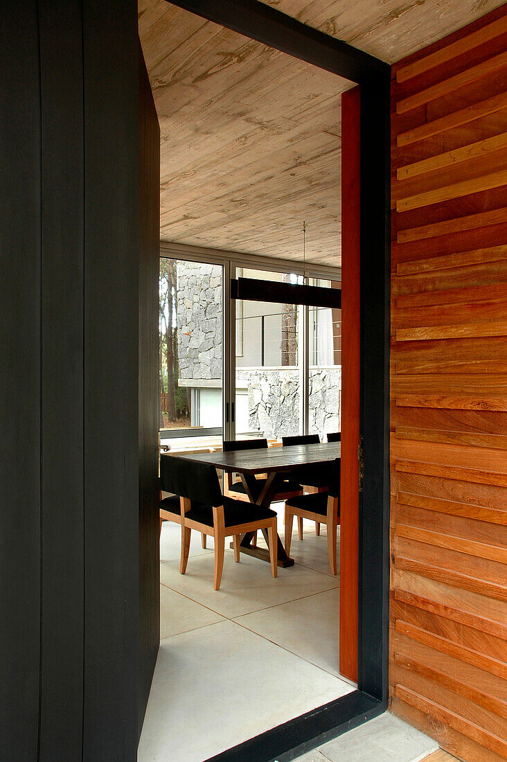 Black front door opens onto modern kitchen dining area of a woodland house with Lapacho wood and black painted cladding