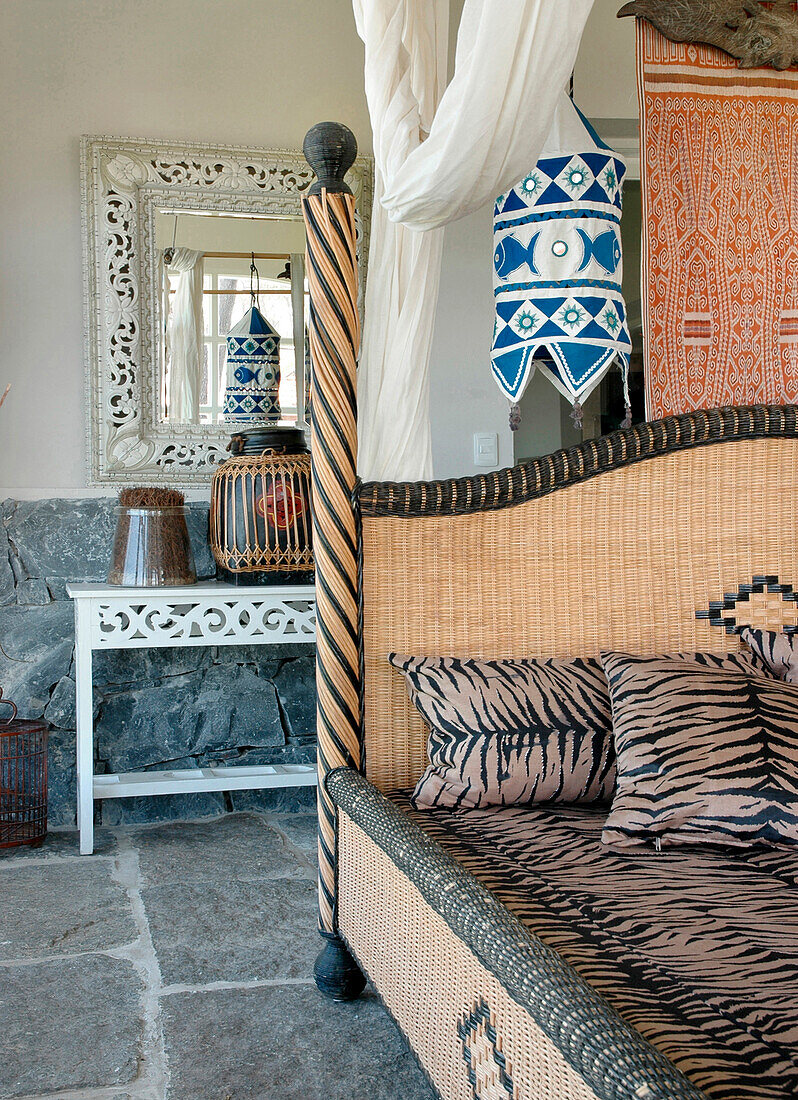 Cane bed with animal print upholstery in bedroom with exposed stone floor