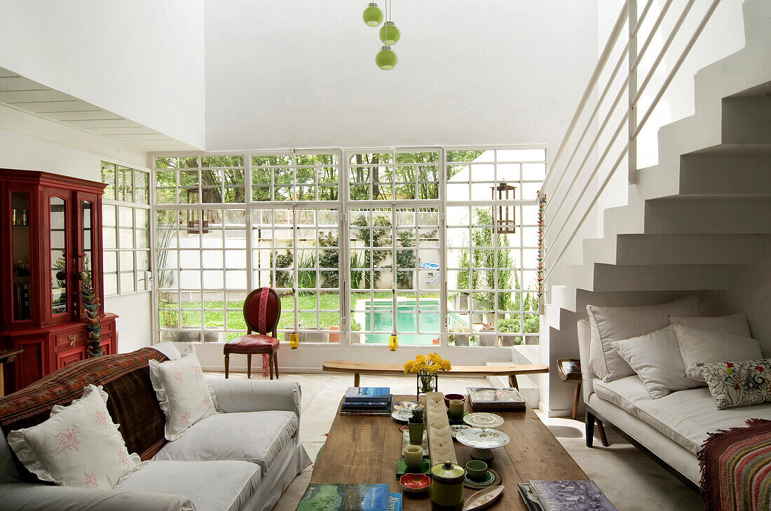 Wohnzimmer mit Tagesbett unter der Treppe, antike Kommode und Blick durch ein großes Fenster in den Garten