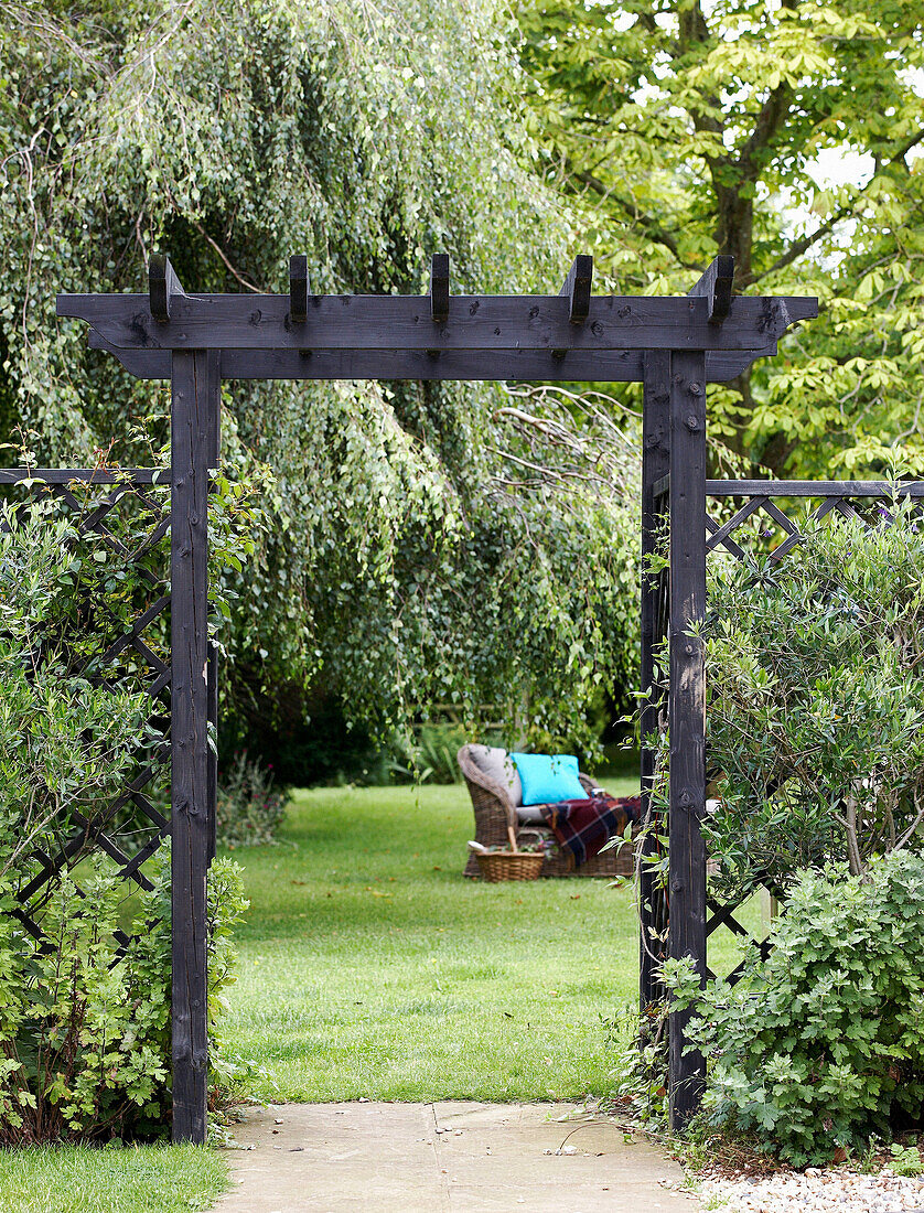 Blick durch einen hölzernen Torbogen auf einen Sitzplatz im Garten mit Rasen