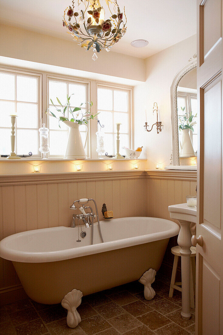 Roll top bath below sunlit bathroom window with lit tealights