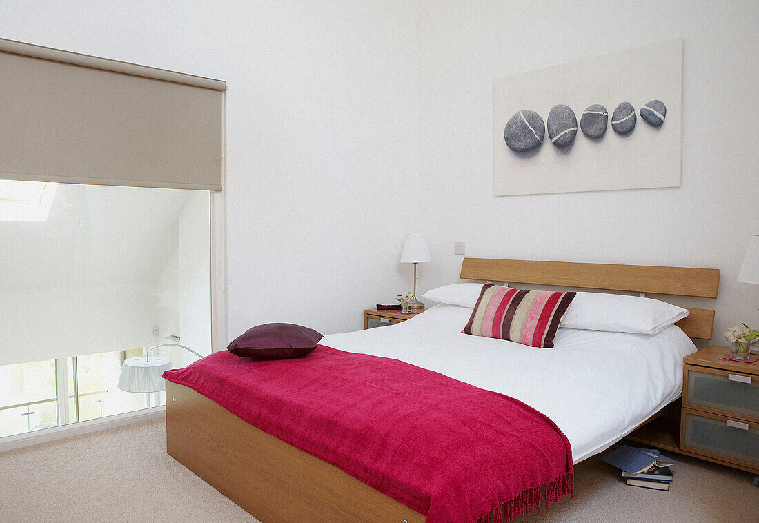 Rosa Decke auf einem Doppelbett in einem Öko-Haus mit großen verglasten Fenstern, durch die die Sonne das Gebäude aufheizt