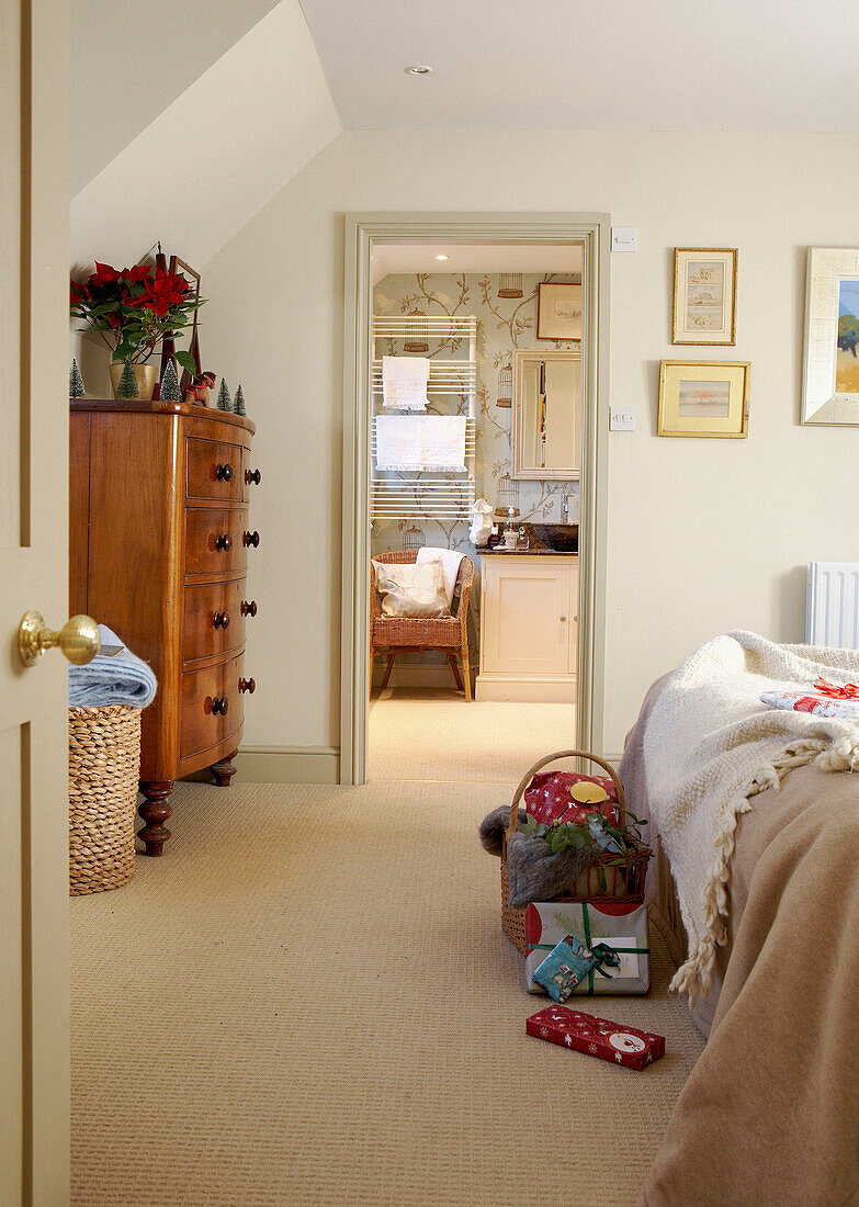 View through doorway of cream bedroom with wooden chest of drawers to ensuite bathroom