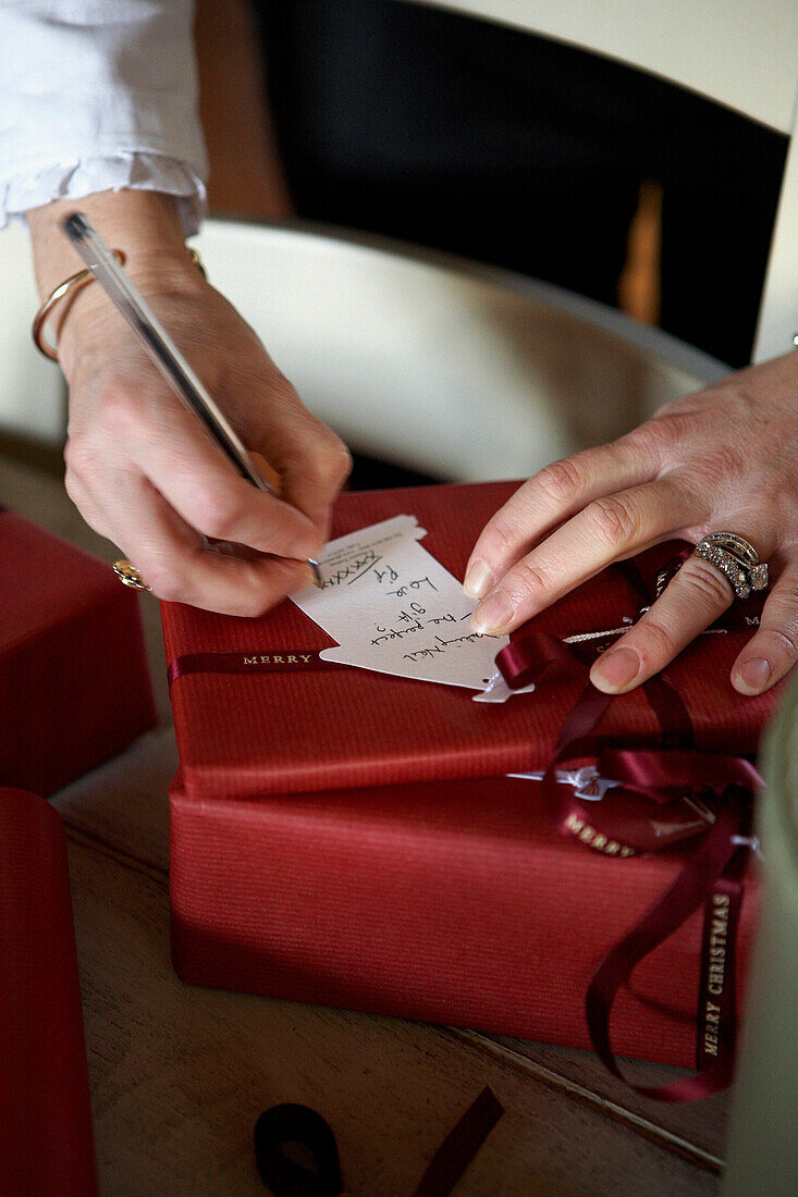 Frau schreibt Geschenkanhänger auf mit Band verpackte Weihnachtsgeschenke