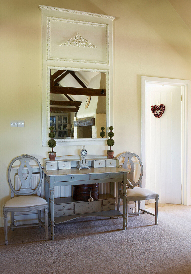 Matching chairs and painted console with square shaped mirror reflecting beamed ceiling