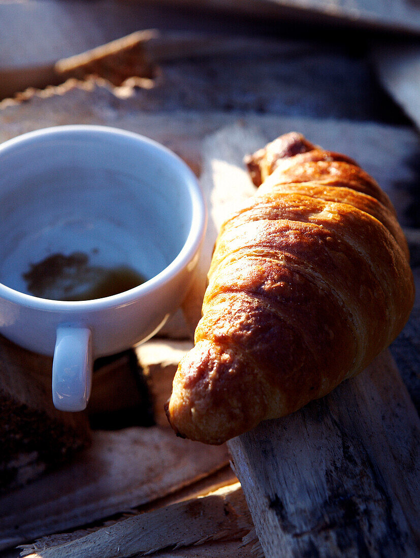 Sunlit croissant and empty coffee cup