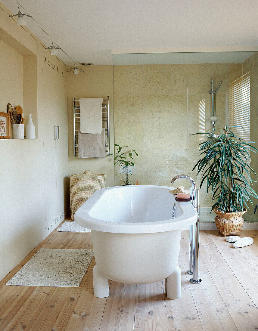 Freestanding bath in sunlit bathroom with wooden floor and glass shower partition 