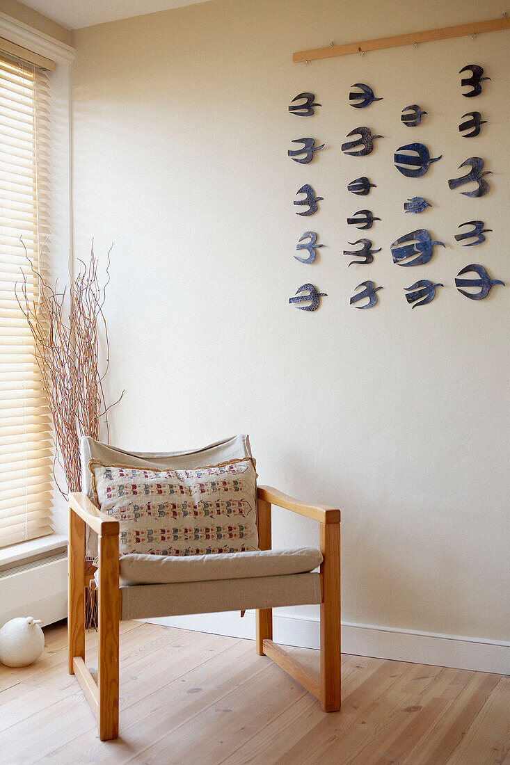 Wood framed chair at sunlit window under marine life art installation 