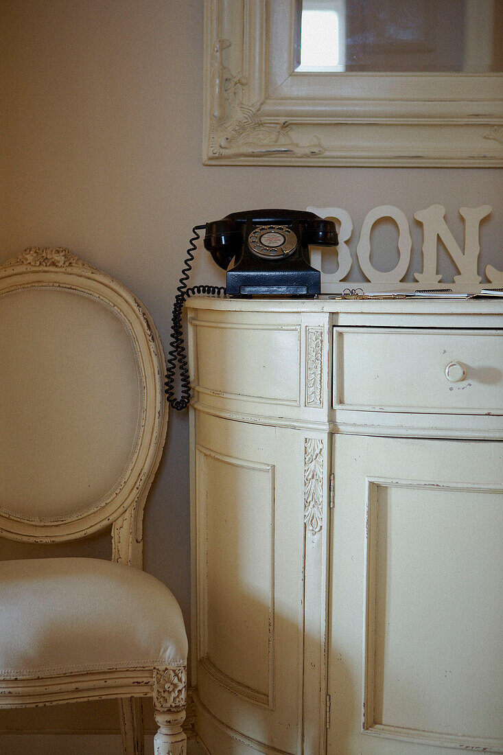 Black rotary dial telephone on cream painted side unit with upholstered chair