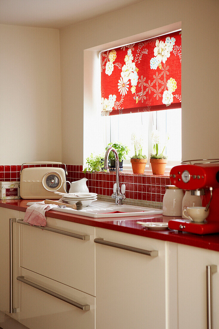 Rot geflieste Küche mit Abwasch und blumengemustertem Rollo