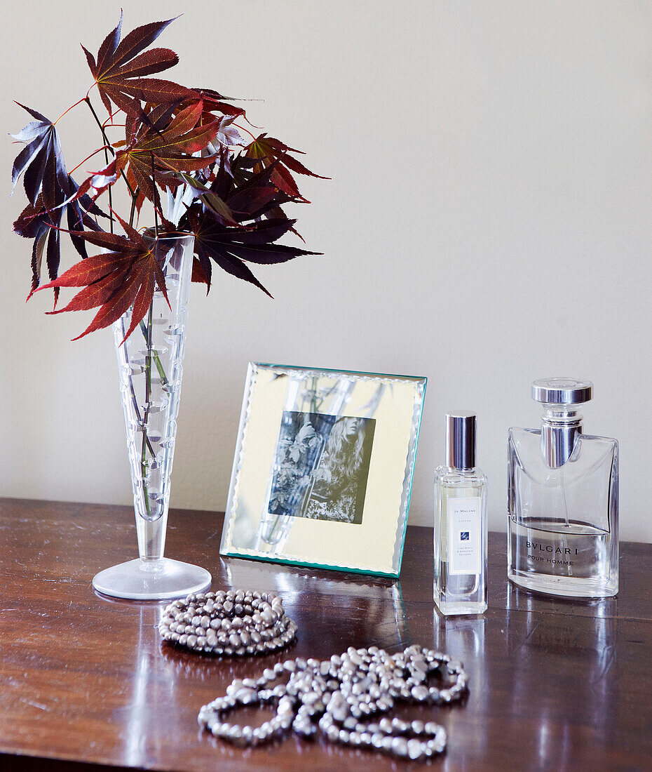 Dried leaves in vase with jewellery and perfume bottles