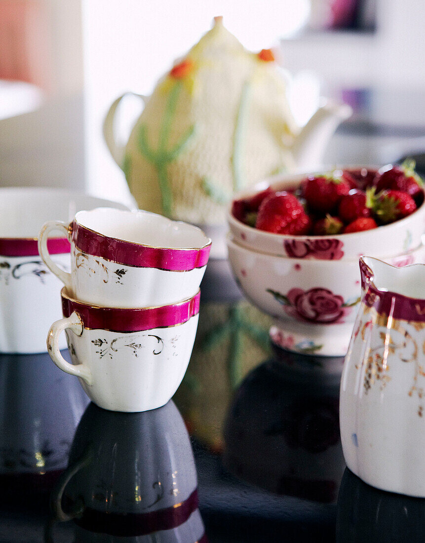 Pretty pink and white china cups and bowls with strawberries on a tabletop