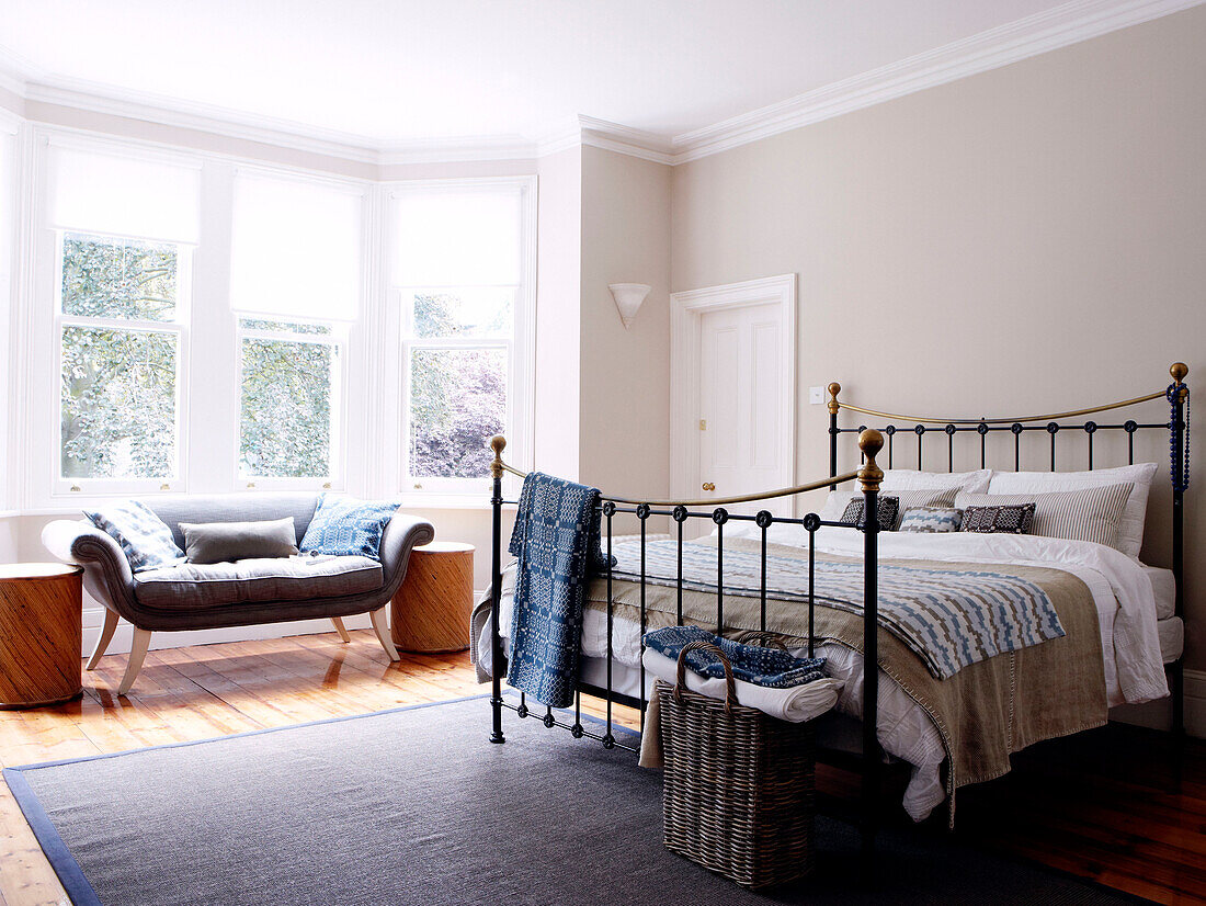 Sunlit bay window of bedroom with fabric on metal framed bed