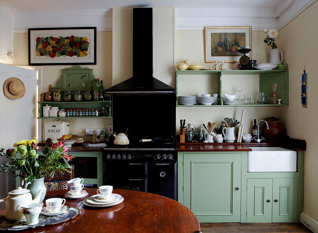 Kitchen diner with black stove and green painted cupboards