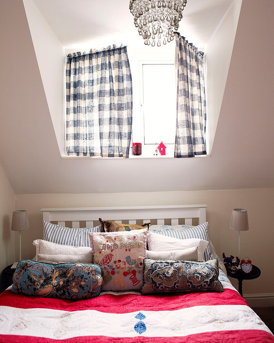 Checked blue and white curtains above bed with pink striped cover and an assortment of cushions