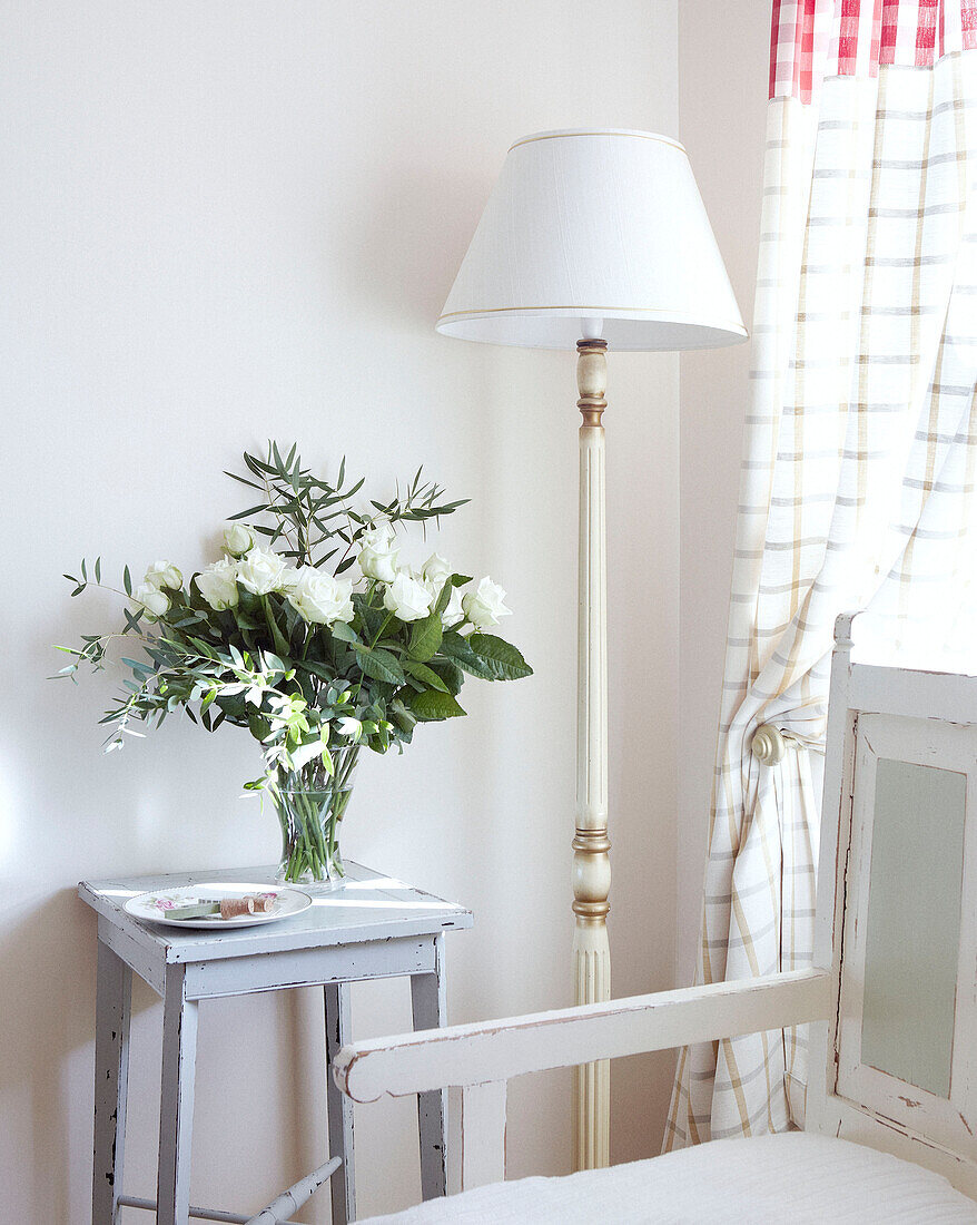 Cut flowers and white standard lamp at window of country home