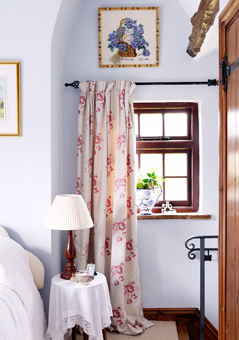 Lampe auf Beistelltisch unter Fenster mit blumengemustertem Vorhang