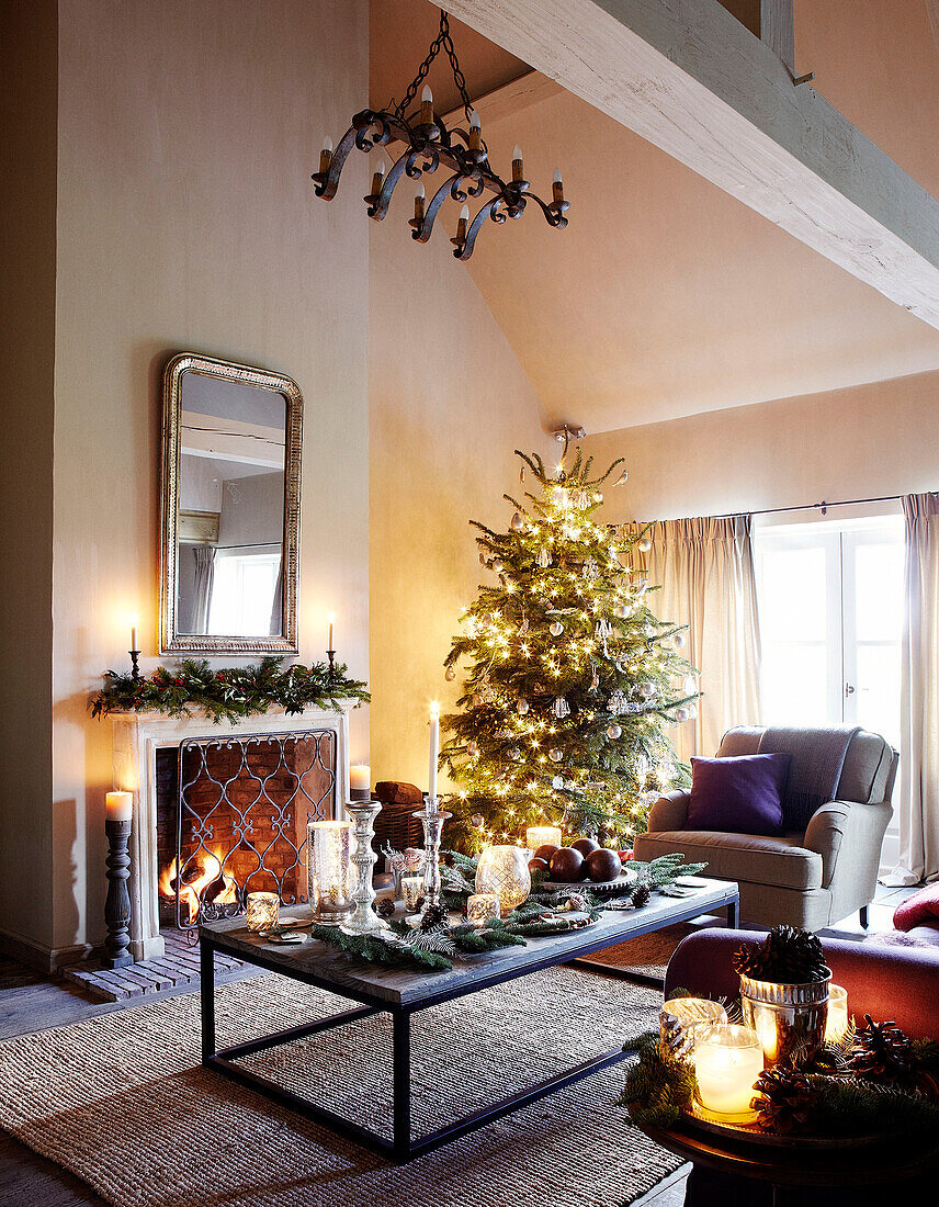 Spiegel über einem beleuchteten Kamin im Wohnzimmer mit beleuchtetem Weihnachtsbaum in einem festlichen Haus in Oxfordshire, England, UK