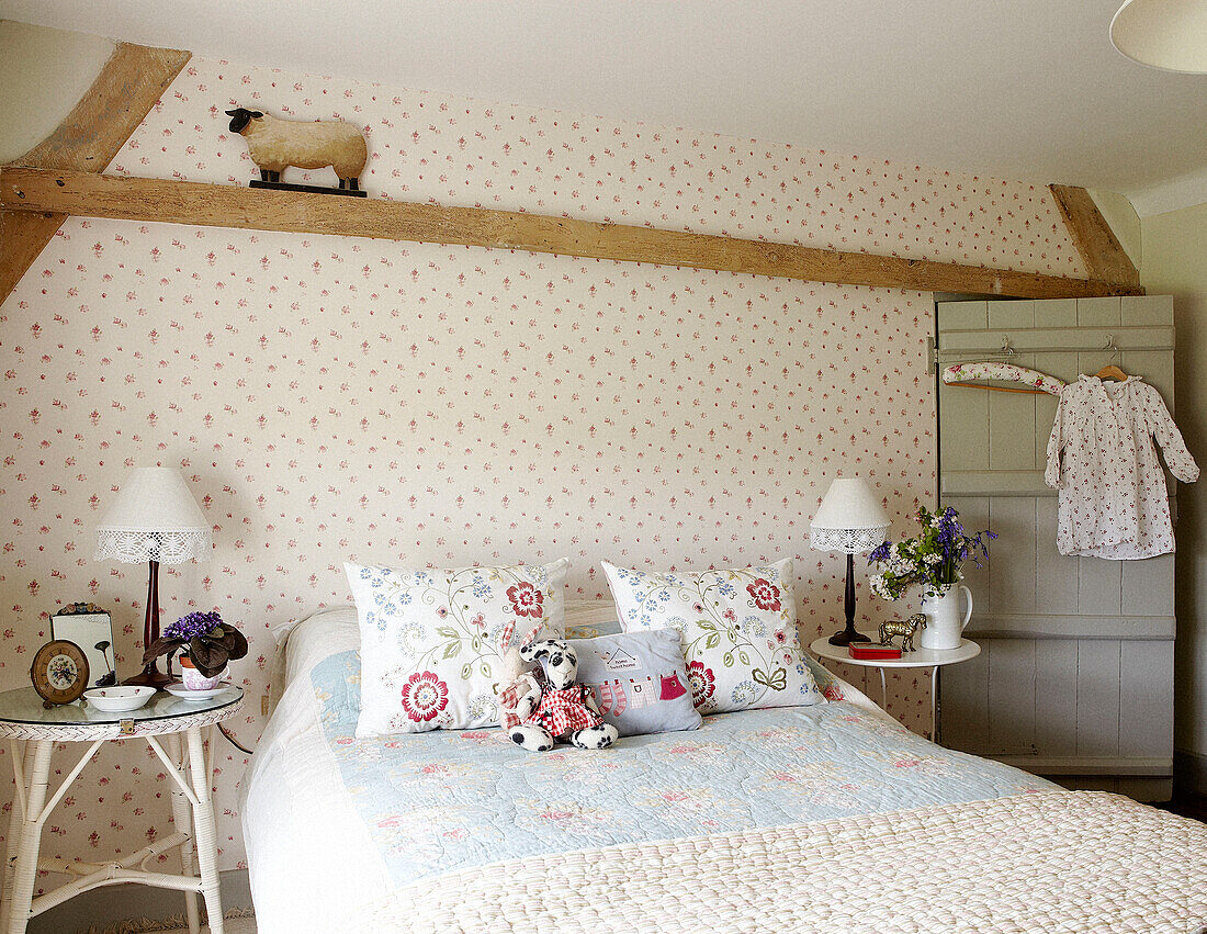Kunstwerk an einer Schlafzimmerwand mit blumenbestickten Kissen und Nachttisch in einem Bauernhaus in Oxfordshire, England, Vereinigtes Königreich