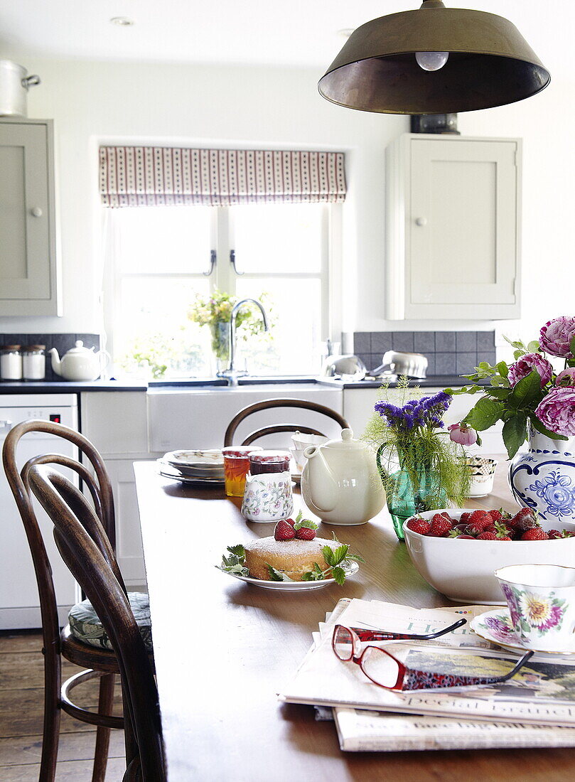 Sponge cake and strawberries with teapot on table in Oxfordshire farmhouse kitchen, England, UK