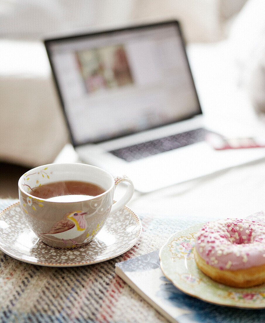 Heißer Tee und ein eisgekühlter Ring Donut mit einem Laptop im Hintergrund in einem Haus in Hastings, East Sussex, Großbritannien