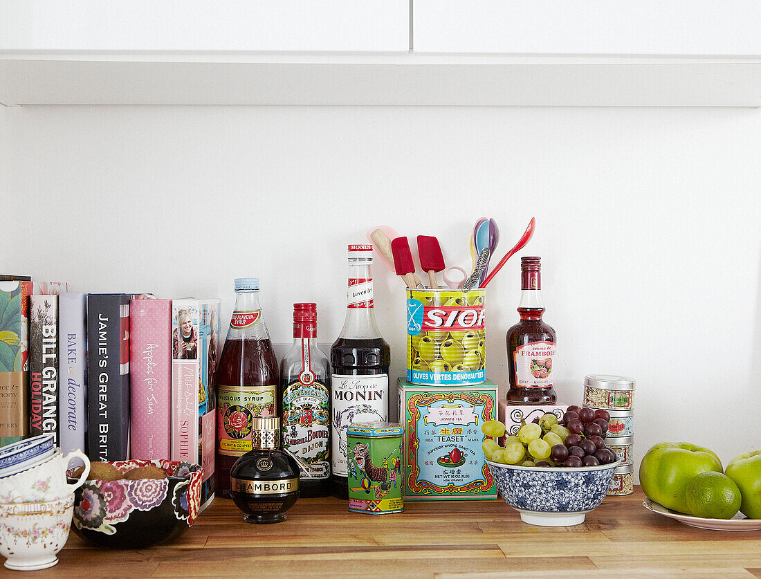 Auswahl an Kochbüchern und Flaschen mit Obst auf hölzernem Küchentisch in einem Haus in Hastings, East Sussex, Großbritannien