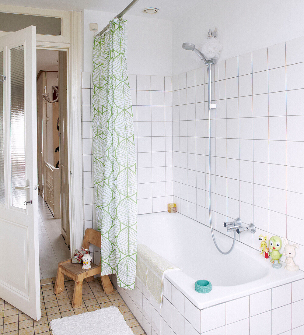 Green patterned shower curtain around bath in white tiled bathroom of family home, Amsterdam, Netherlands