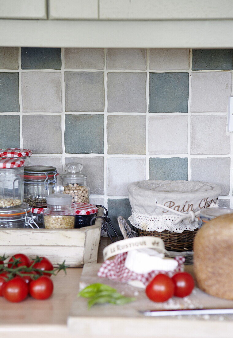 Tomatoes and bread with storage jars on kitchen counter with green tiled splashback, Oxfordshire, England, UK