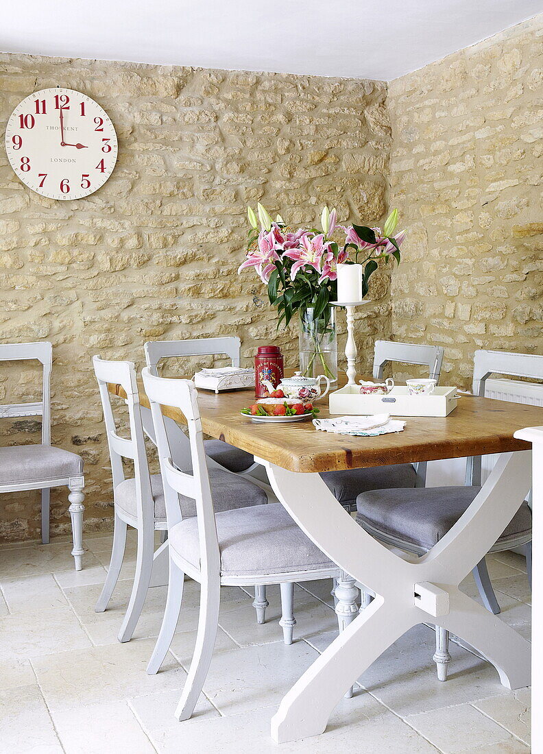 Kitchen table and chairs with clock in exposed stone dining room of barn conversion in Oxfordshire, England, UK