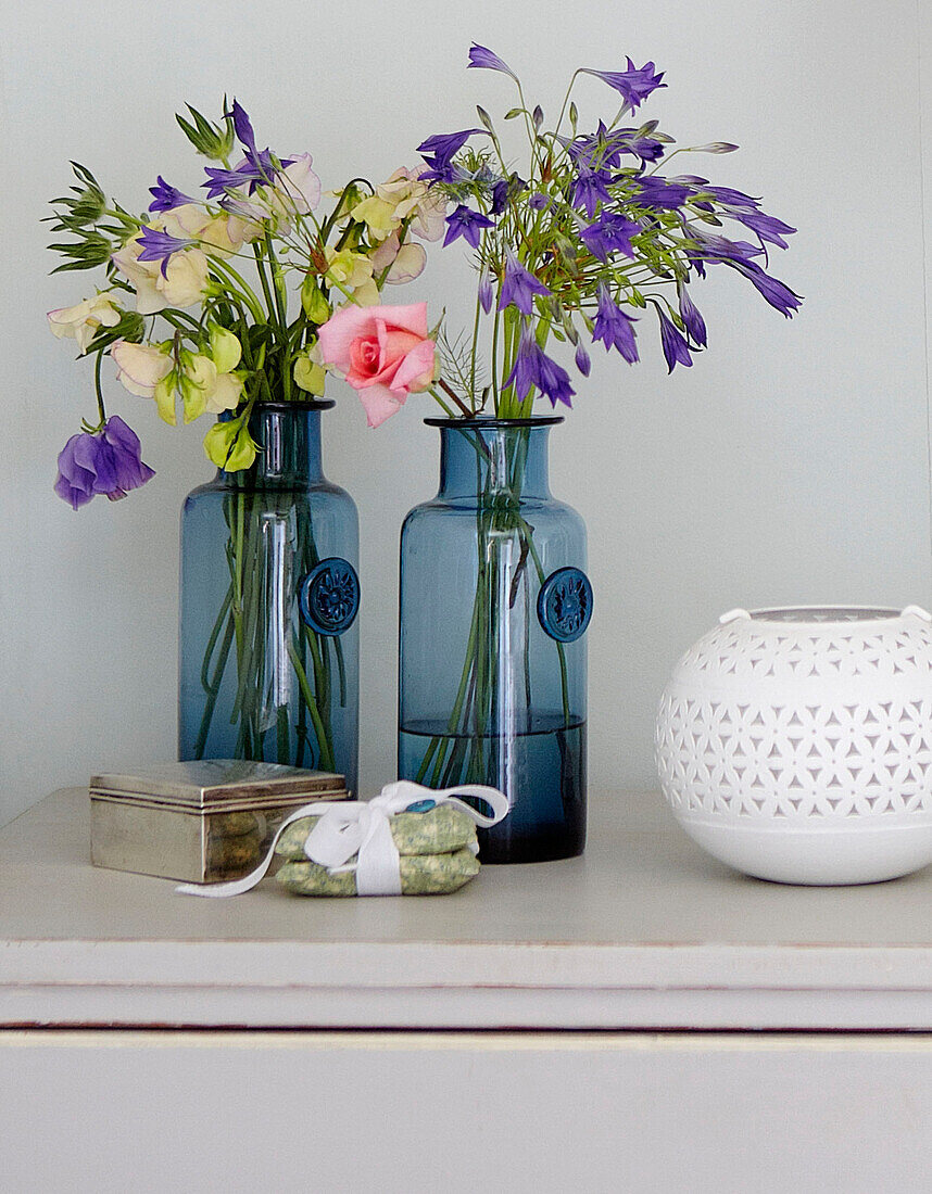 Schnittblumen in blauen Glasvasen mit Kerzenhalter im Schlafzimmer eines Bauernhauses in Surrey, England UK