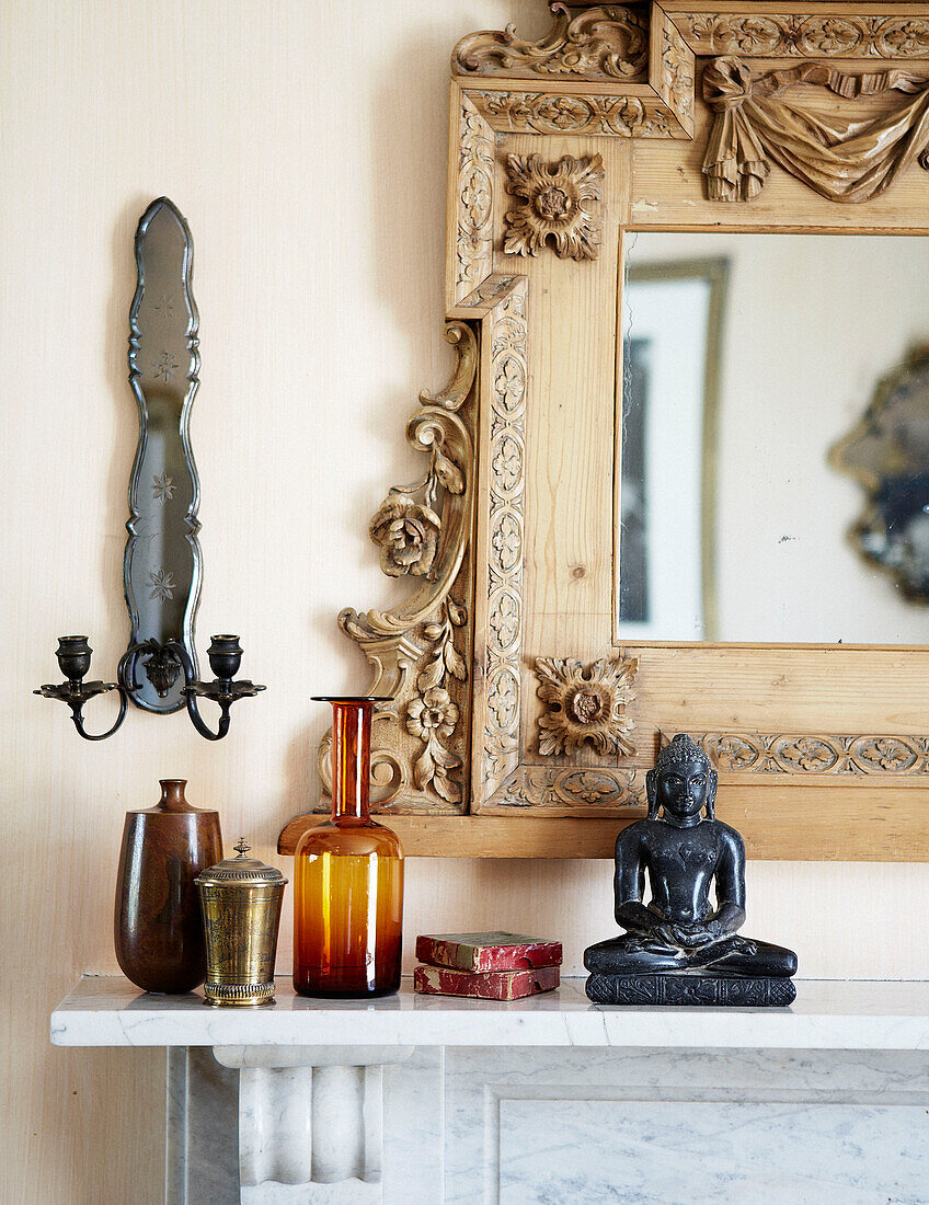 Vintage-Glaswaren und Buddha-Statue mit geschnitztem Spiegelrahmen auf dem Kaminsims in einem Londoner Stadthaus England UK