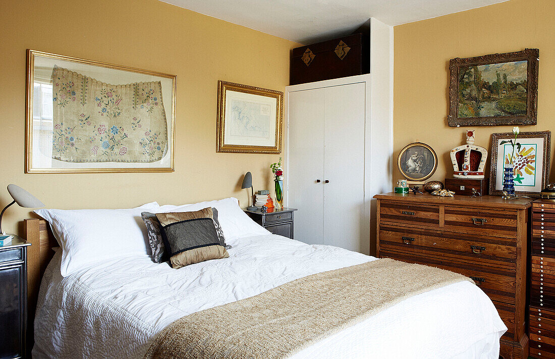 Gilt framed embroidery above double bed with wooden storage drawers in London townhouse England UK