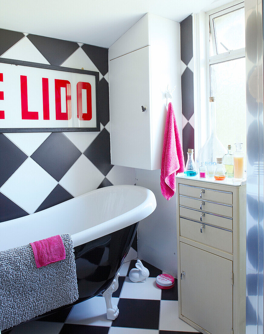 Freistehende Badewanne mit schachbrettartiger Wand und Badezimmerschrank in einem Einfamilienhaus in Margate, Kent, England