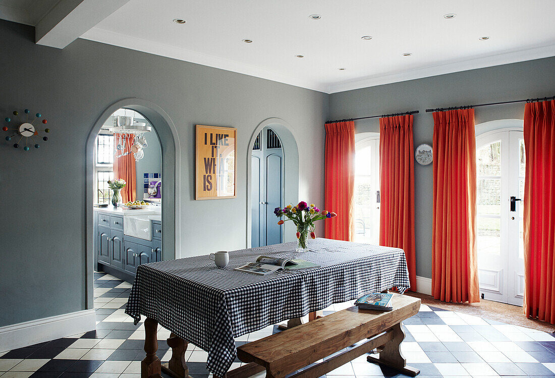 Bright orange curtains with gingham checked tablecloth and arched doorway in Northumbrian manor house England UK