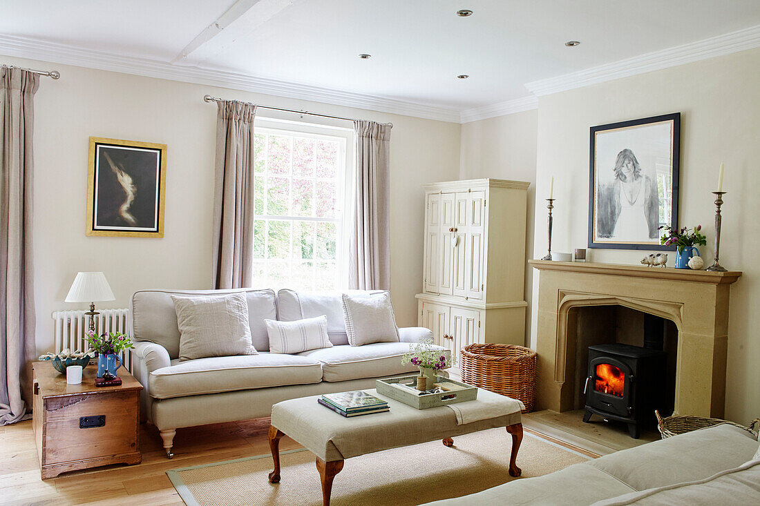 Befeuerter Kaminofen mit Sofa und Ottomane im Wohnzimmer eines Hauses in Northumbria, England, UK