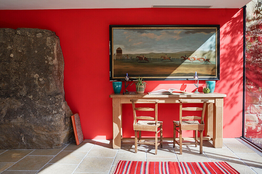 Wooden table and chairs below large artwork with exposed stone in 18th century Northumbrian mill house extension, UK